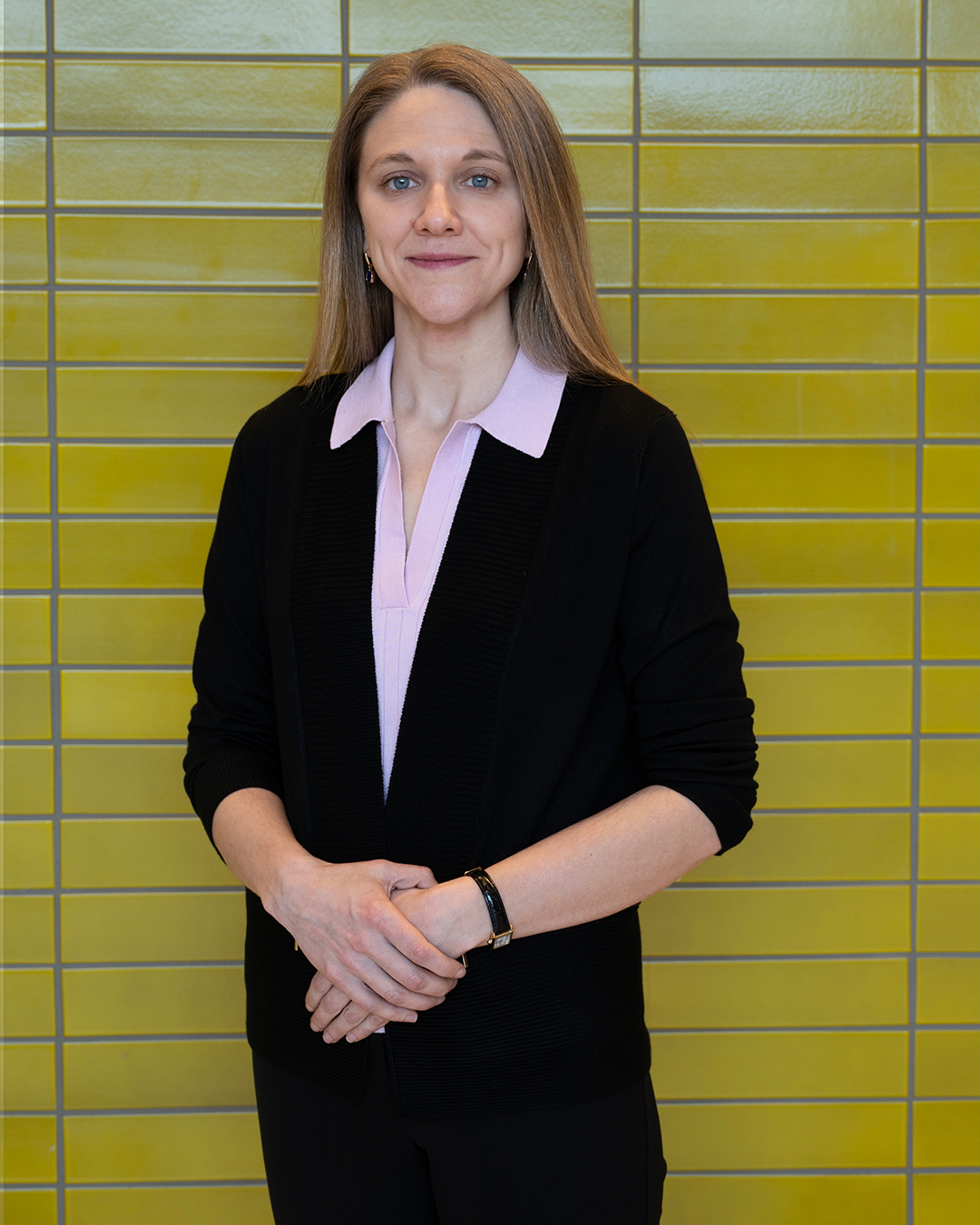Olivia Goosen standing in front of yellow tiled wall, wearing black suit